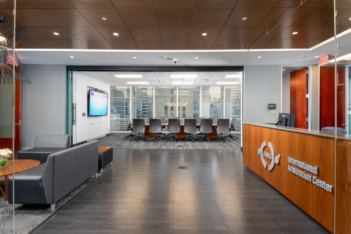 JAMS IAC 16th-floor reception — walnut desk with International Arbitration Center signage, perforated walnut ceiling, lounge seating, arbitration room beyond.