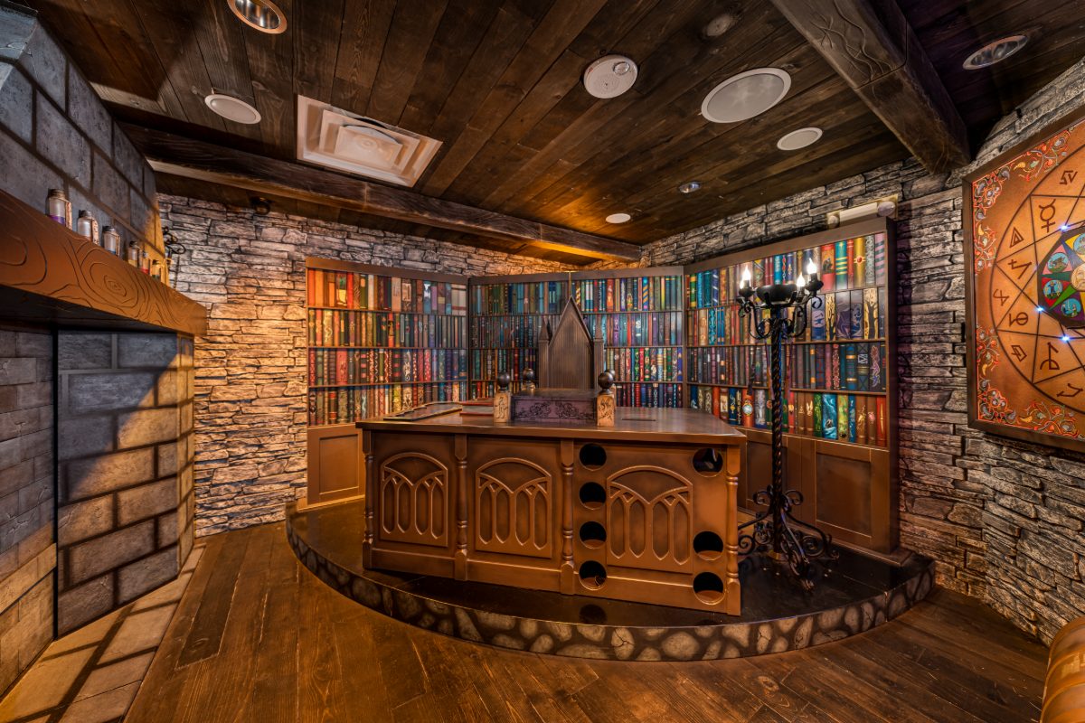 Interior of the Wizard Trials escape room at PanIQ Las Vegas, styled as a wizard's tower study — dark plank ceiling with exposed beams, stone-block and brick walls, a wide-plank fl
